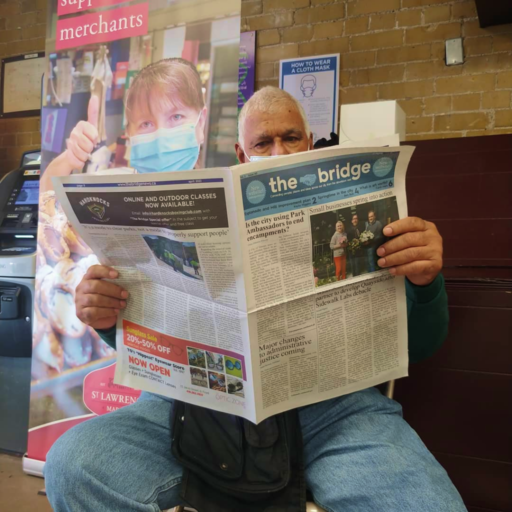 Older gentleman wearing a masks reads the bridge newspaper.